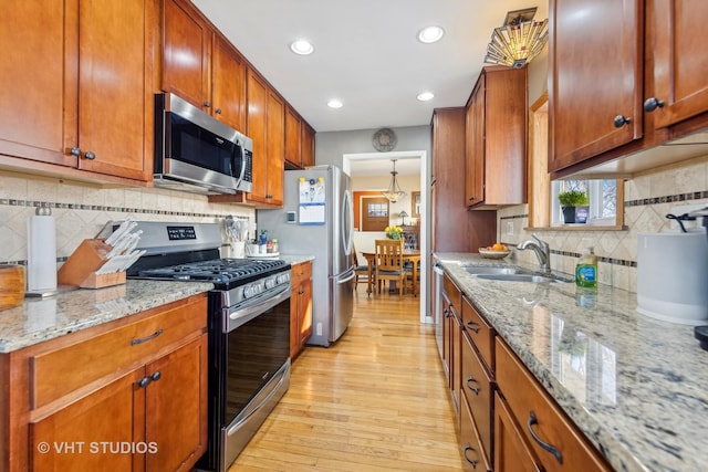 kitchen with sink, light stone counters, light hardwood / wood-style flooring, stainless steel appliances, and decorative backsplash