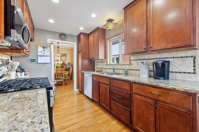 kitchen with appliances with stainless steel finishes, tasteful backsplash, sink, light stone counters, and light hardwood / wood-style flooring