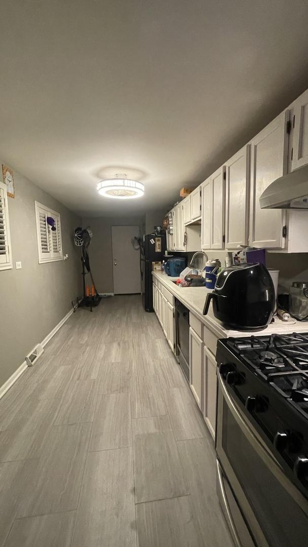 kitchen featuring light countertops, freestanding refrigerator, gas range, under cabinet range hood, and baseboards