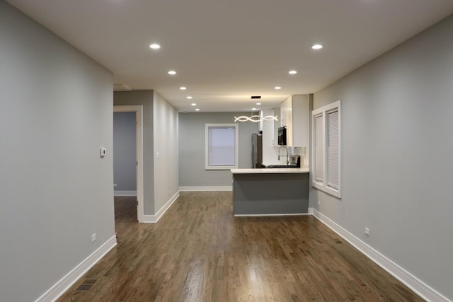 interior space featuring white cabinetry, kitchen peninsula, stainless steel fridge, dark wood-type flooring, and sink