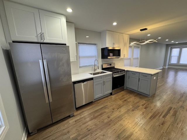 kitchen with kitchen peninsula, stainless steel appliances, gray cabinetry, pendant lighting, and sink