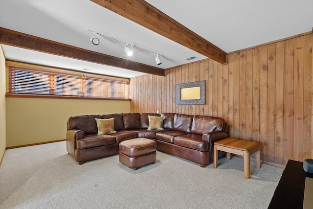 carpeted living room featuring track lighting, beam ceiling, and wood walls