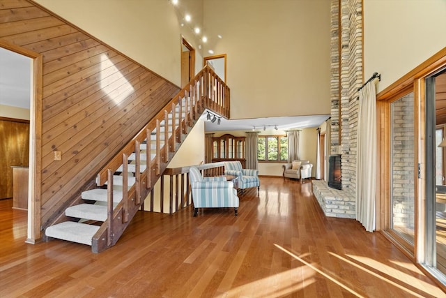 unfurnished living room with a brick fireplace, hardwood / wood-style flooring, wood walls, and a high ceiling