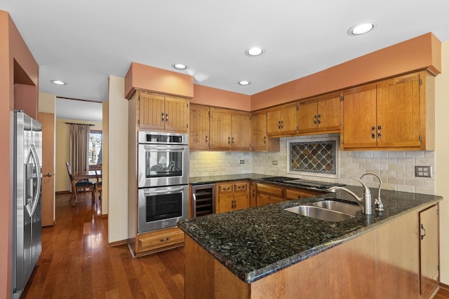 kitchen with appliances with stainless steel finishes, sink, wine cooler, dark stone counters, and kitchen peninsula