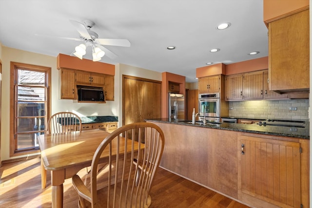 kitchen with sink, light hardwood / wood-style flooring, dark stone countertops, stainless steel appliances, and kitchen peninsula