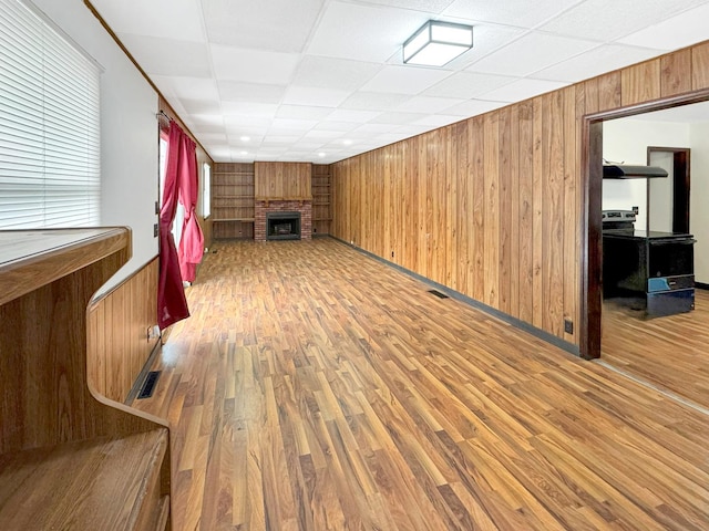 unfurnished living room with a drop ceiling, wood-type flooring, a fireplace, and wood walls