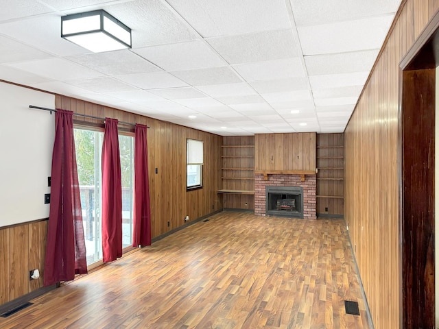 unfurnished living room with hardwood / wood-style flooring, built in shelves, a drop ceiling, and a fireplace