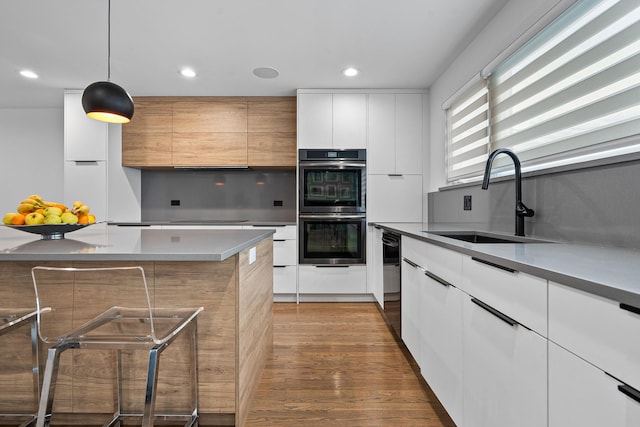 kitchen with double oven, white cabinetry, sink, hanging light fixtures, and dark wood-type flooring