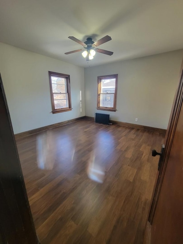 empty room featuring ceiling fan, dark hardwood / wood-style floors, and radiator heating unit