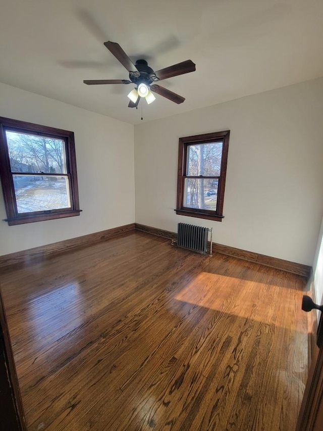 empty room featuring ceiling fan, dark hardwood / wood-style flooring, and radiator heating unit