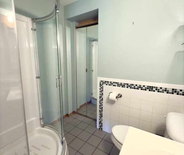 bathroom featuring toilet, an enclosed shower, tile patterned flooring, and tile walls