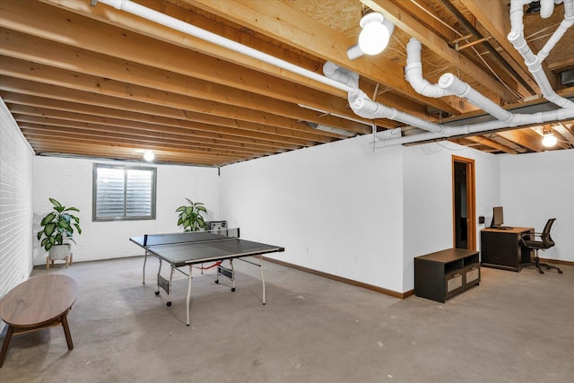 recreation room with brick wall, concrete floors, and baseboards