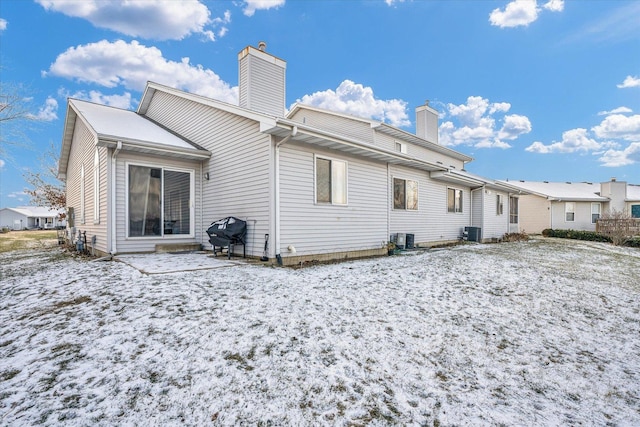 snow covered rear of property featuring central air condition unit and a chimney