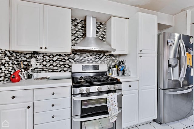 kitchen with appliances with stainless steel finishes, white cabinets, tasteful backsplash, light tile patterned floors, and wall chimney range hood