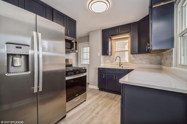 kitchen featuring a sink, light countertops, appliances with stainless steel finishes, light wood-type flooring, and backsplash