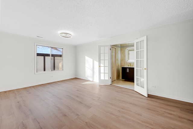 empty room with ornamental molding, a textured ceiling, light wood-type flooring, and french doors