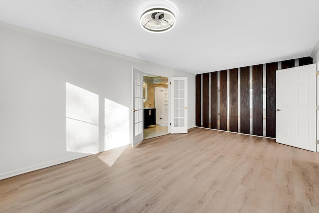 unfurnished living room featuring ornamental molding, french doors, a textured ceiling, and light wood-type flooring