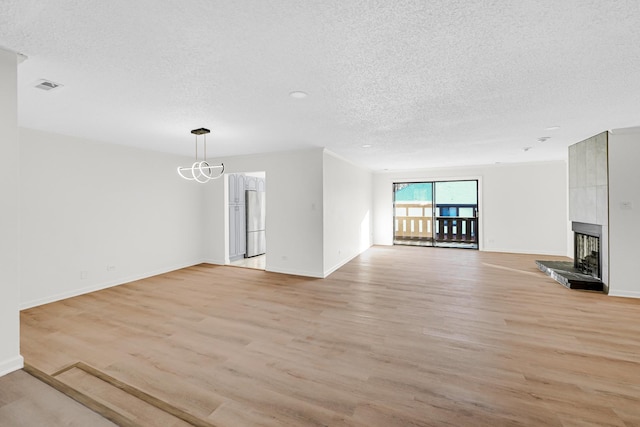 unfurnished living room with a large fireplace, light hardwood / wood-style floors, a textured ceiling, and a notable chandelier