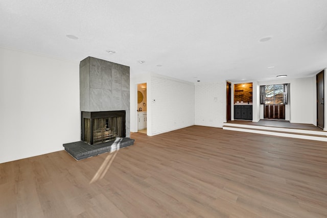 unfurnished living room with a multi sided fireplace, brick wall, wood-type flooring, and a textured ceiling