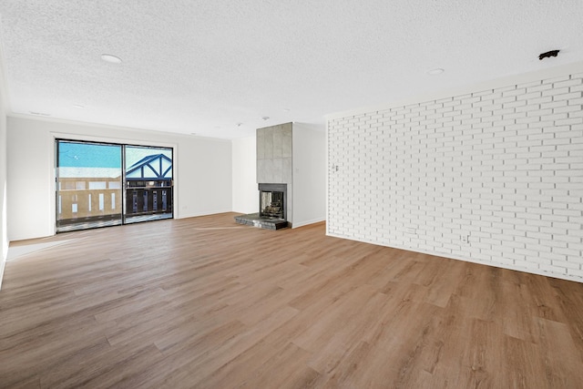 unfurnished living room featuring a large fireplace, brick wall, a textured ceiling, and light wood-type flooring