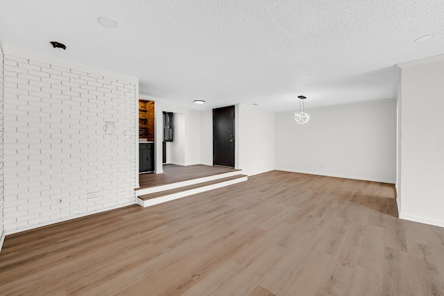 unfurnished living room with brick wall, a textured ceiling, and light hardwood / wood-style flooring