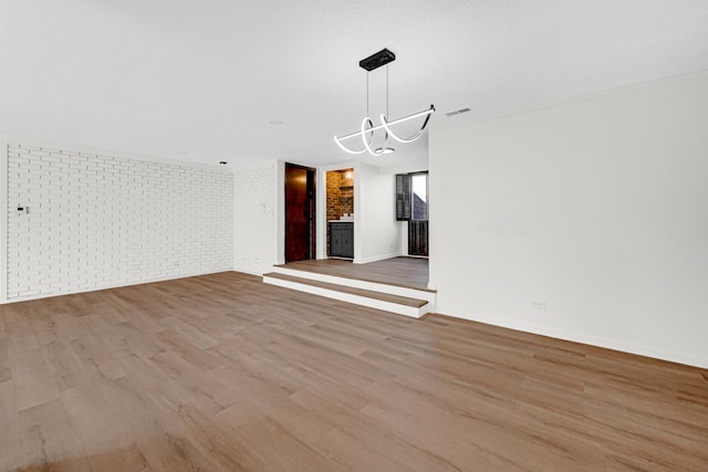 unfurnished dining area featuring a chandelier, light hardwood / wood-style flooring, ornamental molding, brick wall, and a fireplace