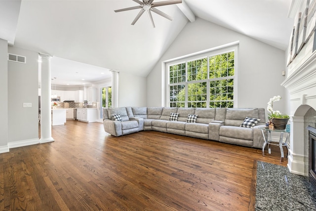 living area with visible vents, high vaulted ceiling, a glass covered fireplace, dark wood finished floors, and decorative columns