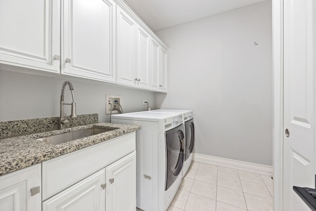 laundry area featuring light tile patterned floors, baseboards, cabinet space, a sink, and washer and clothes dryer