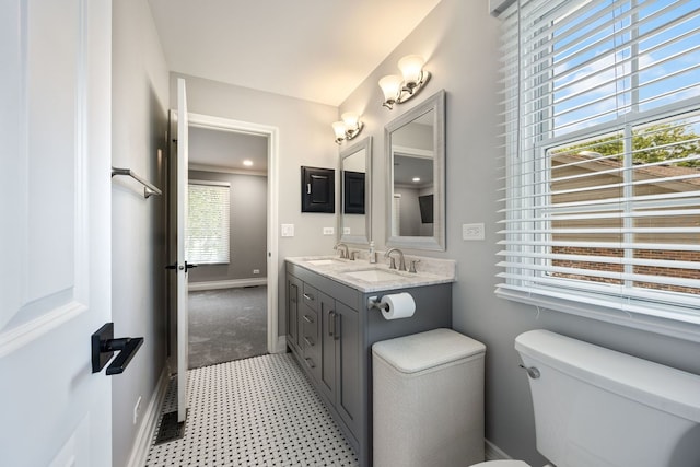 bathroom with double vanity, toilet, baseboards, and a sink