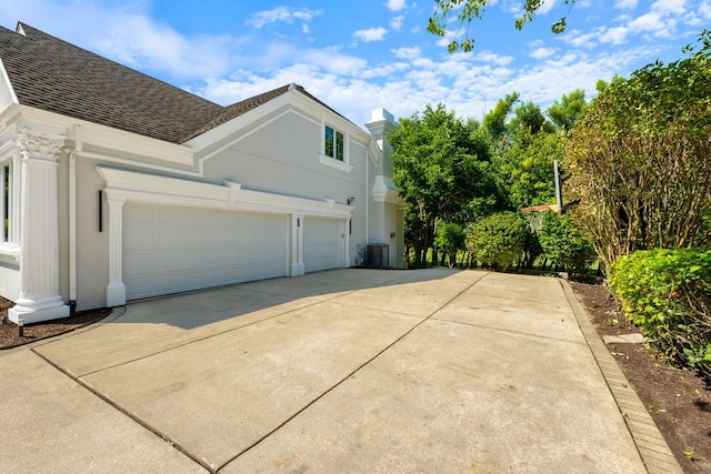 view of side of home with an attached garage, central AC unit, driveway, and roof with shingles