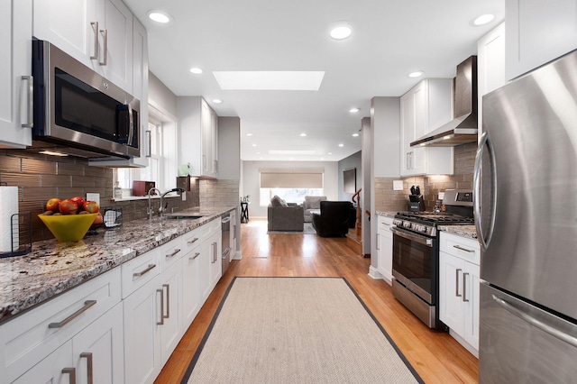 kitchen with wall chimney exhaust hood, white cabinets, and appliances with stainless steel finishes