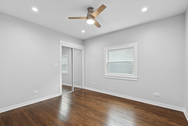 unfurnished bedroom with ceiling fan, multiple windows, dark hardwood / wood-style floors, and a closet