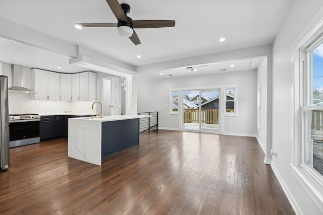 kitchen with a kitchen island with sink, stainless steel appliances, dark hardwood / wood-style floors, white cabinets, and wall chimney exhaust hood