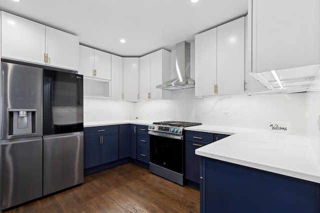 kitchen featuring dark wood-type flooring, blue cabinetry, white cabinetry, stainless steel appliances, and wall chimney range hood