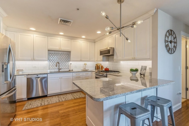 kitchen featuring sink, appliances with stainless steel finishes, white cabinetry, decorative light fixtures, and kitchen peninsula