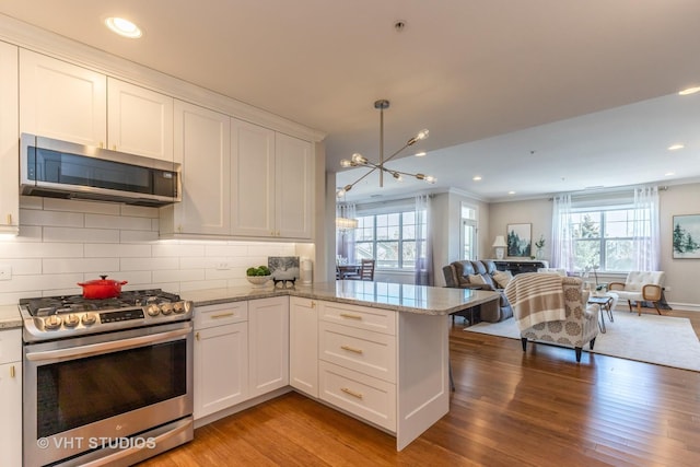 kitchen featuring appliances with stainless steel finishes, white cabinetry, hanging light fixtures, kitchen peninsula, and a healthy amount of sunlight