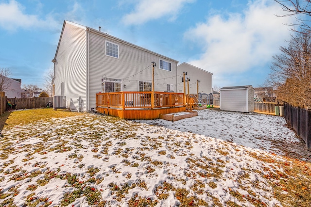 snow covered back of property with a deck and a shed