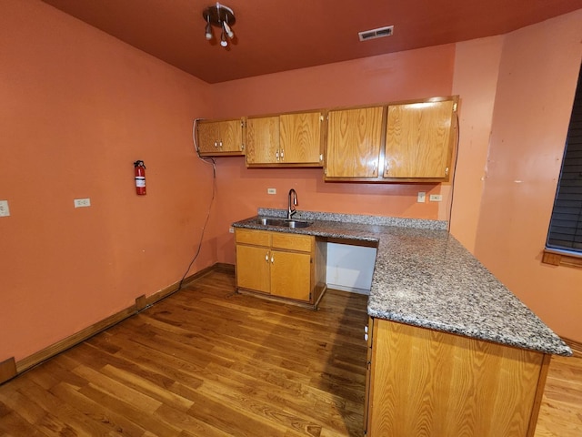 kitchen with kitchen peninsula, dark hardwood / wood-style flooring, sink, and stone counters