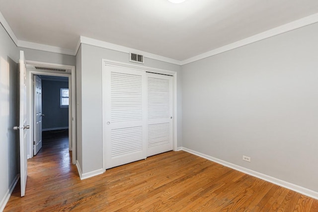 unfurnished bedroom featuring a closet, crown molding, and hardwood / wood-style floors