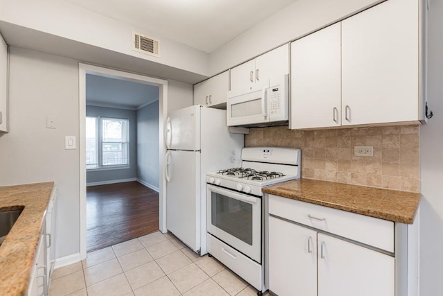 kitchen featuring white appliances, white cabinets, dark stone countertops, decorative backsplash, and light tile patterned floors