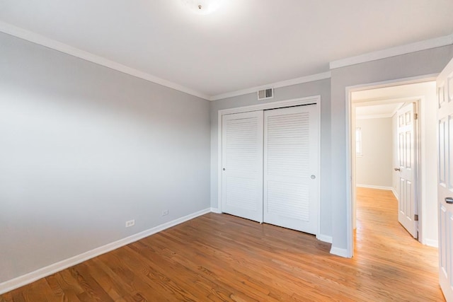 unfurnished bedroom with a closet, crown molding, and light hardwood / wood-style floors