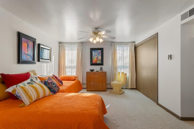 bedroom featuring baseboard heating, light colored carpet, ceiling fan, and a closet