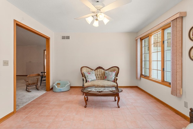 living area featuring light tile patterned floors, ceiling fan, visible vents, and baseboards