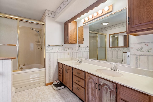 bathroom featuring double vanity, combined bath / shower with glass door, a sink, and wallpapered walls