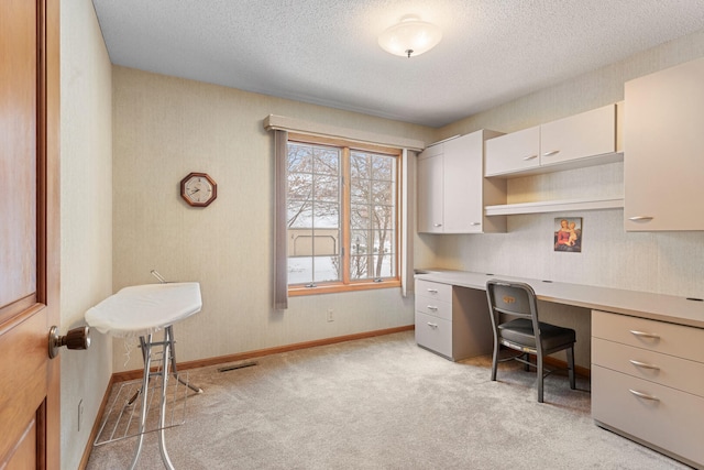 carpeted home office featuring built in desk and a textured ceiling