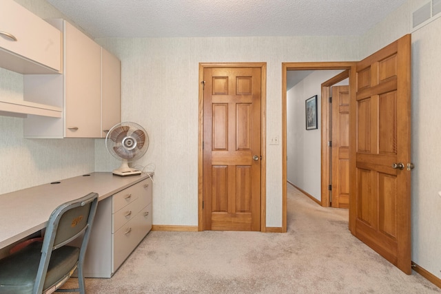 office featuring light carpet, baseboards, visible vents, built in study area, and a textured ceiling