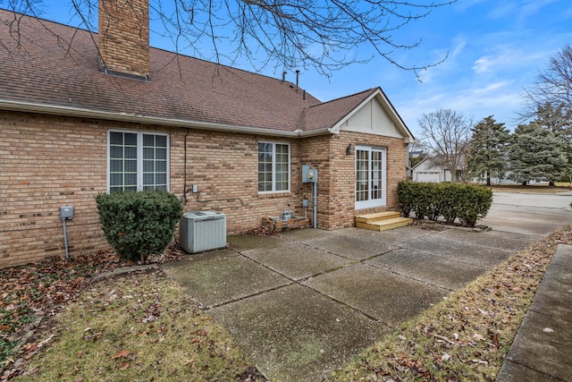 back of house featuring entry steps, a chimney, roof with shingles, central AC, and brick siding