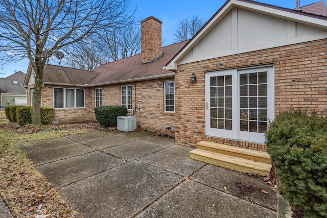 rear view of property with entry steps, a patio, a chimney, central air condition unit, and brick siding