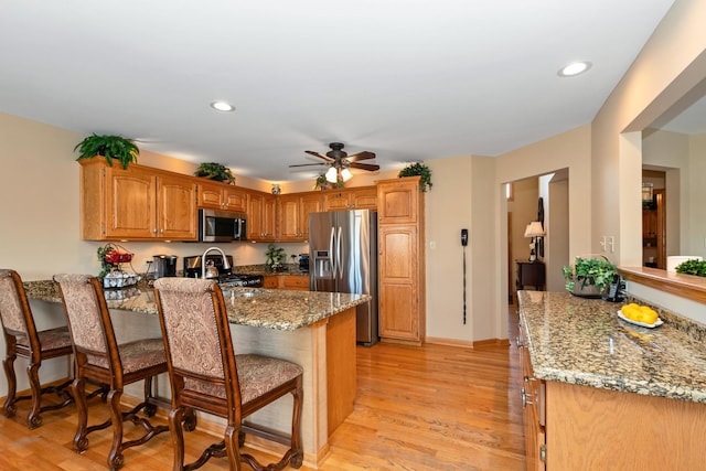 kitchen featuring light wood-type flooring, kitchen peninsula, appliances with stainless steel finishes, and a breakfast bar