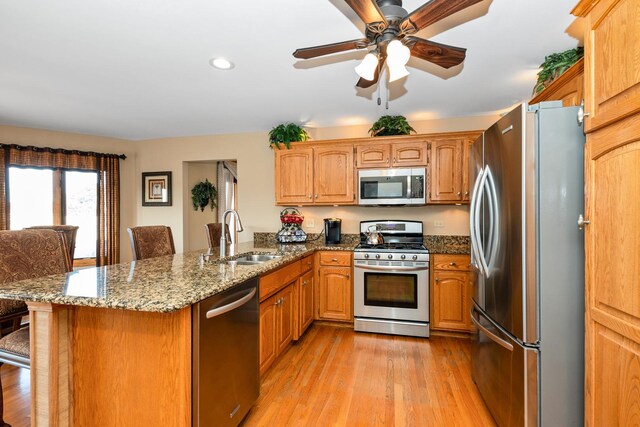 kitchen with sink, light wood-type flooring, kitchen peninsula, stainless steel appliances, and stone countertops